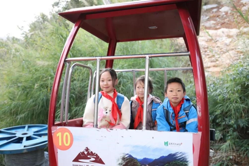 Para pelajar dari kampung Sungai Nizhu sedang menaiki kereta kabel. (Foto oleh Jia Liyao)